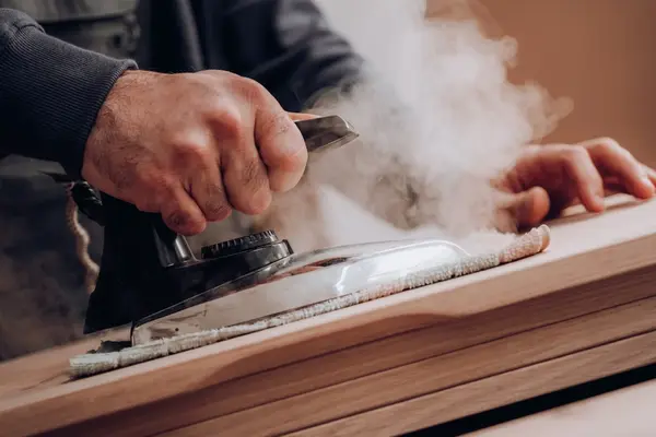 Handwerker bügelt dampfend Holzoberfläche, Möbelbau und Holzpflege Nahaufnahme