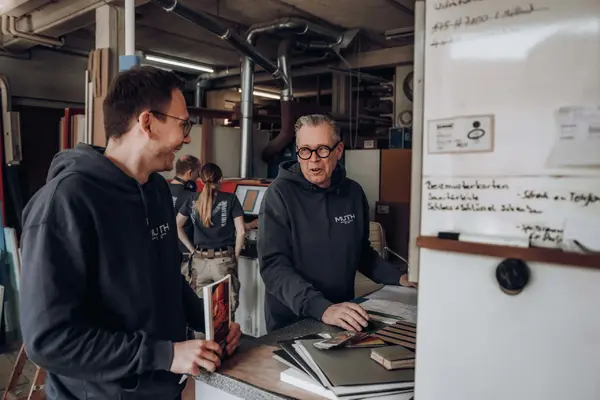 Mitarbeiter beraten Kunden in Schreinerei-Werkstatt am Tresen, Musterplatten