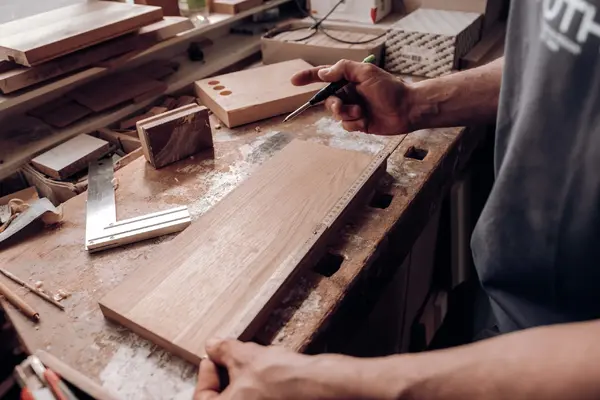 Schreiner markiert Holzbrett auf Werkbank mit Winkel und Maßstab.