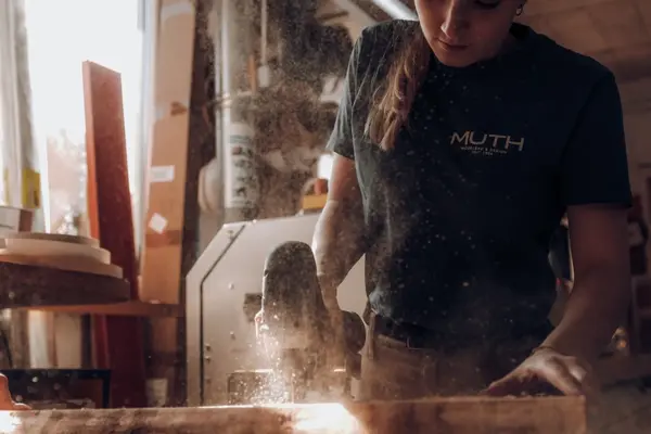 Schreinerin sägt Holzbrett in der Werkstatt, Staub fliegt beim Möbelbau
